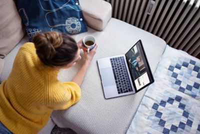 Donna con computer sdraiata sul letto vista dall'alto mentre beve un caffè