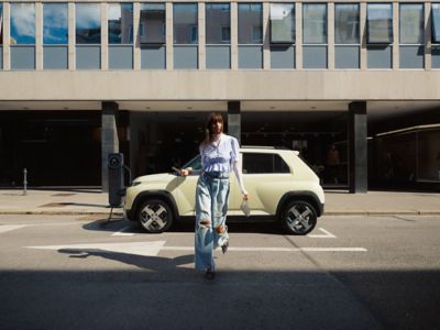 Ein Frau vor einem parkenden Hyundai INSTER am Straßenrand.