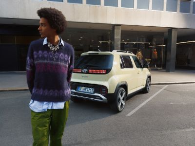 A man standig in front of rear view of the Hyundai INSTER small electric car.