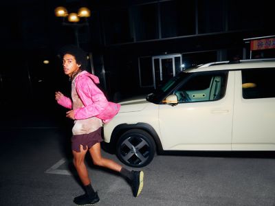 A woman in a pink jacket walks past the new Hyundai INSTER small electric car.