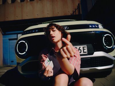 A woman sitting in front of the grille of the Hyundai INSTER small electric car.