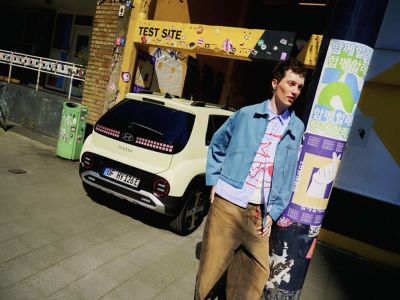 Un homme debout à côté d'un lampadaire devant l'arrière de la nouvelle petite voiture électrique Hyundai INSTER.