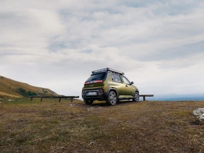 Hyundai INSTER Cross parked on grass near wooden benches under an overcast sky.