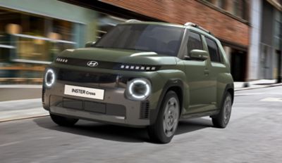 Driekwart vooraanzicht van Hyundai INSTER Cross rijdend in een stadstraat.