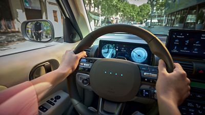 Driver view with hands on wheel, blind-spot camera and side-mirror alert showing a person on a bicycle.