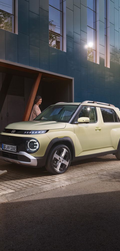 Hyundai INSTER parked on a city sidewalk while two people walk past a modern building.
