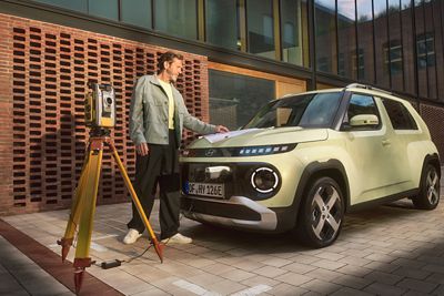 Person consulting plans beside the INSTER with a tripod instrument nearby and a cable connected to the vehicle.