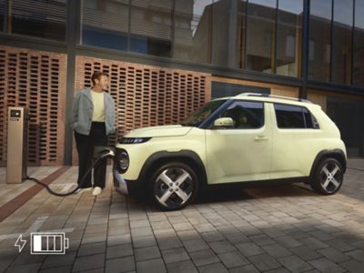 Person stands next to the INSTER while it charges at a public charging station in an urban plaza.