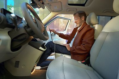 Person seated inside using a laptop powered via the vehicle's interior V2L outlet with a cable connected.