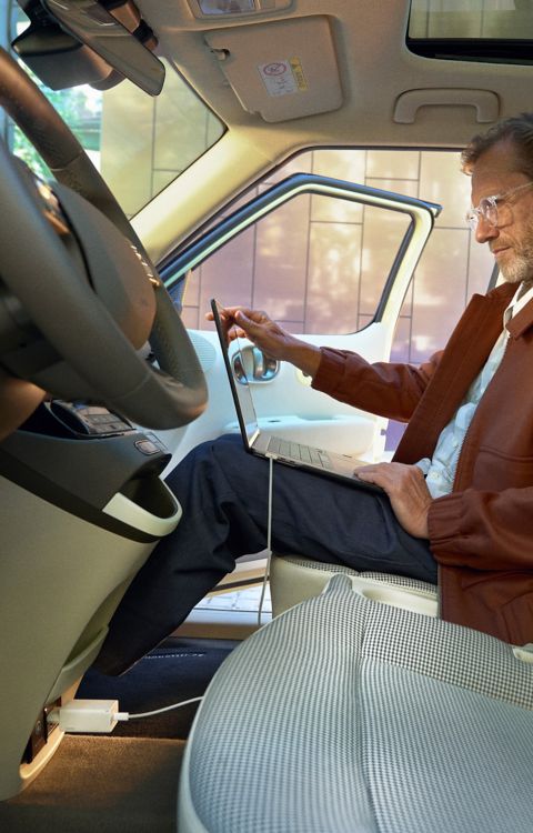 Person seated inside using a laptop powered via the vehicle's interior V2L outlet with a cable connected.