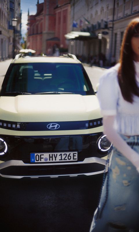 Woman standing in front of a Hyundai INSTER small electric car in a city.