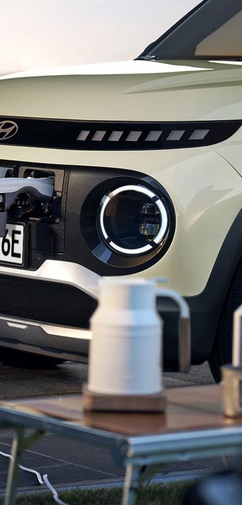 Front of Hyundai INSTER with its V2L Vehicle to Load cable powering a speaker and electric kettle.