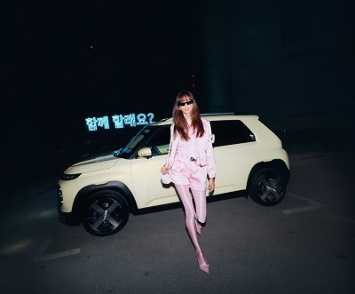 A woman in pink walking away from the new Hyundai INSTER small electric car parked on the street.