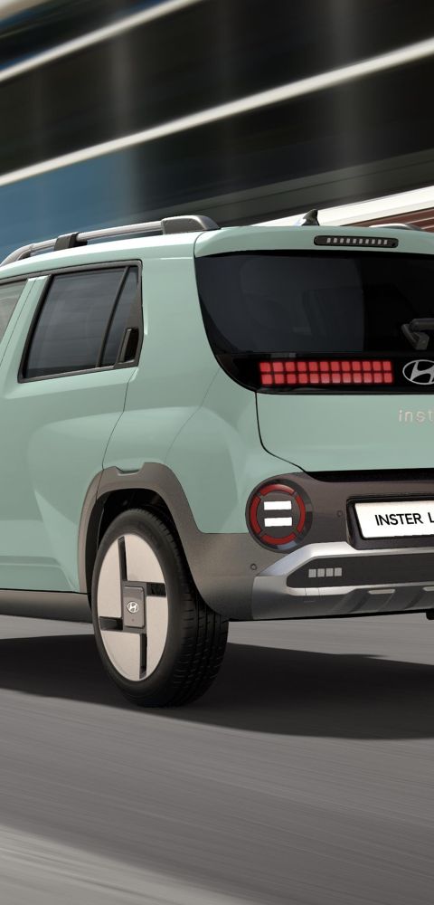 The Hyundai INSTER Lounge in Glow Mint shown from the rear driving down a city street.