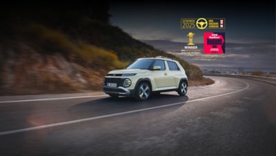 A Hyundai INSTER electric SUV drives on a winding road, with award badges including "Golden Steering Wheel 2025", "World Electric Vehicle 2025", and "TopGear Supermini of the Year 2026" displayed in the top right.