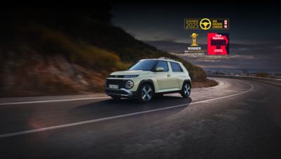 Una donna in piedi accanto a un lampione, di fronte a Hyundai INSTER