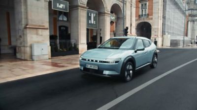 Hyundai IONIQ 3 in Ice Pearl Blue driving through an urban street.