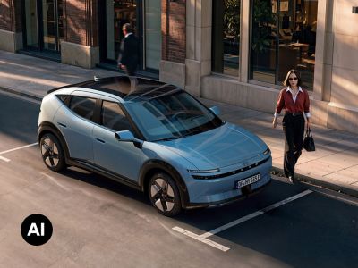 A woman walking next to Hyundai IONIQ 3 in Ice Blue Pearl parked on the city street.