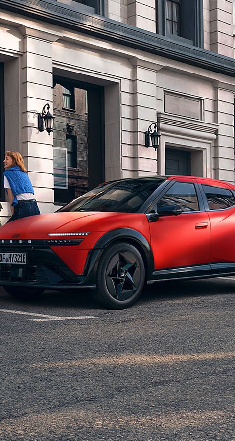 Muž a žena stojící vedle červeného Hyundai IONIQ 3 zaparkovaného v městské ulici.