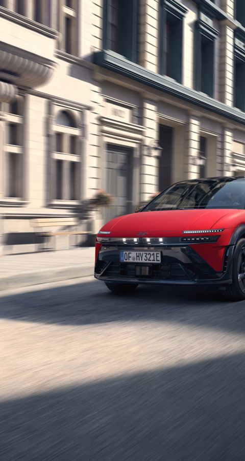  Röd Hyundai IONIQ 3 parkerad i sidovy på en gata, med ett galleri bakom bilen.