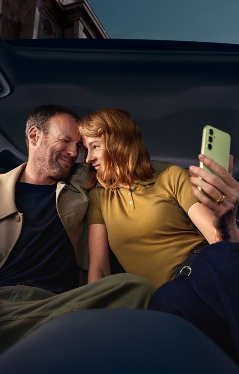 Ein Mann und eine Frau mit Smartphone in der Hand sitzen auf dem Rücksitz des Hyundai IONIQ 3.