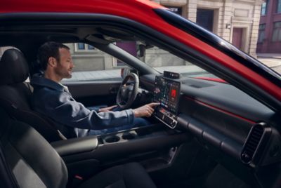 Red Hyundai IONIQ 3 parked side view on a street, with a gallery behind the car.