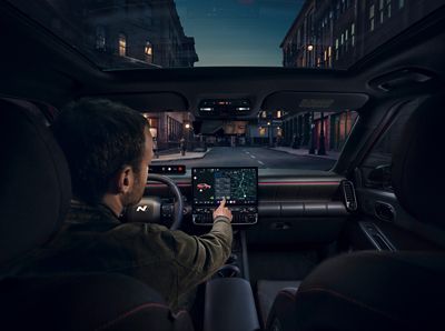 Red Hyundai IONIQ 3 parked side view on a street, with a gallery behind the car.