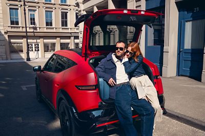 Red Hyundai IONIQ 3 with open luggage compartment showing suitcases on a city street.