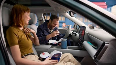 A man and a woman eating take out food in the front seats of the Hyundai IONIQ 3.