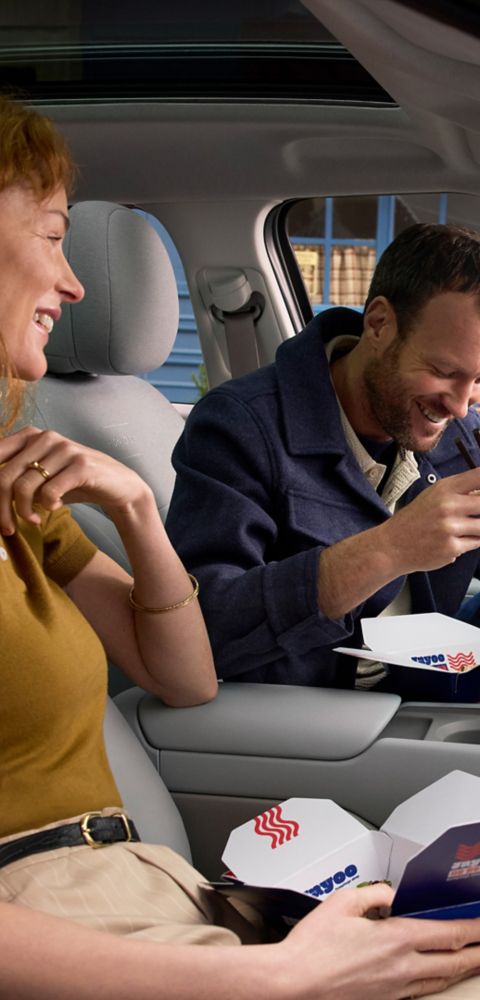 A man and a woman eating take out food in the front seats of the Hyundai IONIQ 3.
