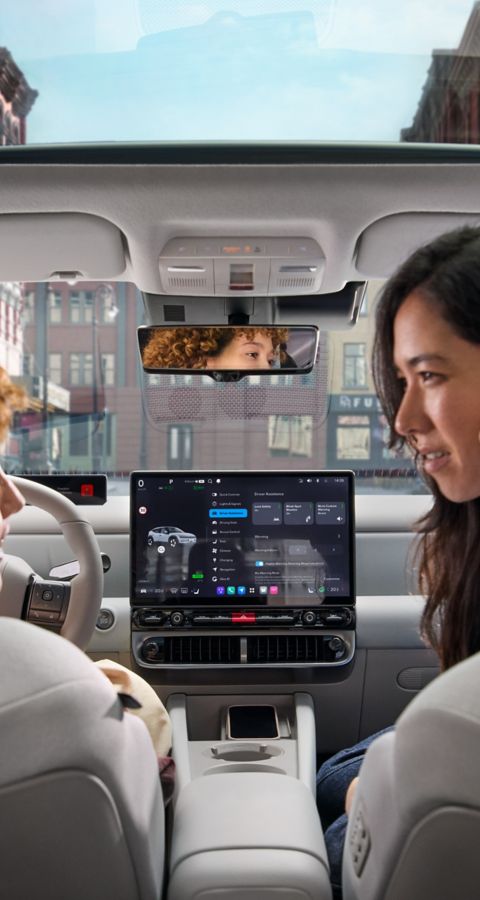 Two woman relaxing and talking in the front seats of the Hyundai IONIQ 3 with the sun roof visible.