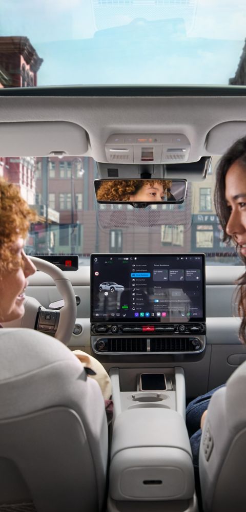 Two woman relaxing and talking in the front seats of the Hyundai IONIQ 3 with the sun roof visible.