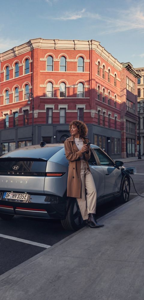 Hyundai IONIQ 3 charging on a city street with a woman leaning on the rear bumper.