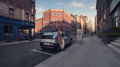 Hyundai IONIQ 3 charging on a city street with a woman leaning on the rear bumper.