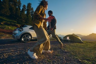 Two people by a Hyundai IONIQ 5 and tent at sunset in the mountains.