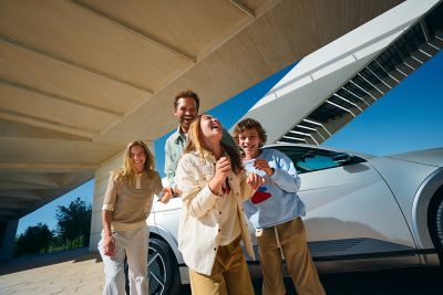 A family stands in front of a Hyundai IONIQ 5 with a modern building behind them.