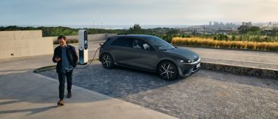 En man  går från en parkerad Hyundai IONIQ 5 elbil som laddar med vy över stad i  bakgrunden.