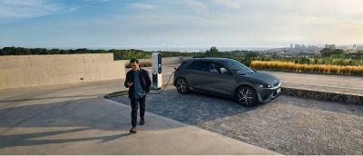  En man  går från en parkerad Hyundai IONIQ 5 elbil som laddar med vy över stad i  bakgrunden.