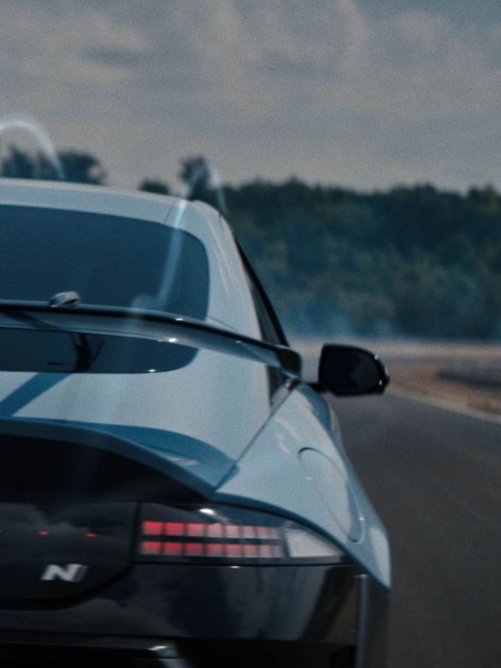 Rear view of a Hyundai IONIQ 6 N on a track, showcasing dynamic aerodynamics with smoke trailing behind.