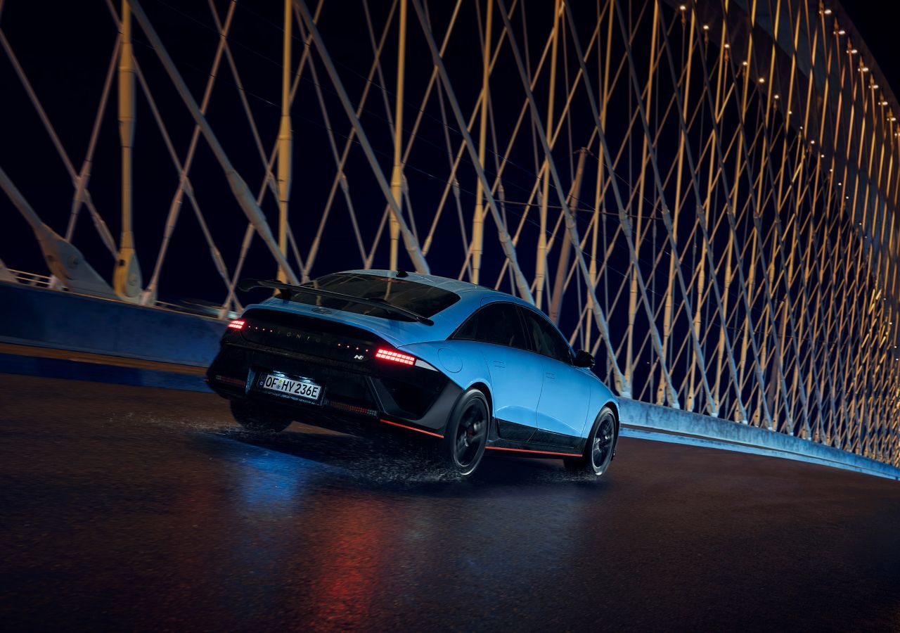 A Hyundai IONIQ 6 N drives across a bridge at night, surrounded by illuminated architectural elements.