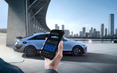 Eine Hand, die ein Smartphone hält, auf dem der Ladezustand des Hyundai IONIQ 6 N mit einem Auto und einer Stadtsilhouette angezeigt wird.