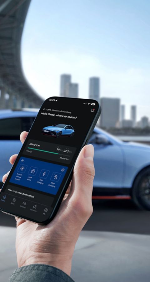 Hand holding smartphone displaying Hyundai IONIQ 6N charging status with car and city skyline.