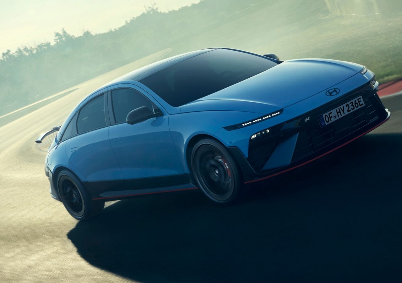 A Hyundai IONIQ 6 N powers through a track corner, showcasing its performance in a misty environment.