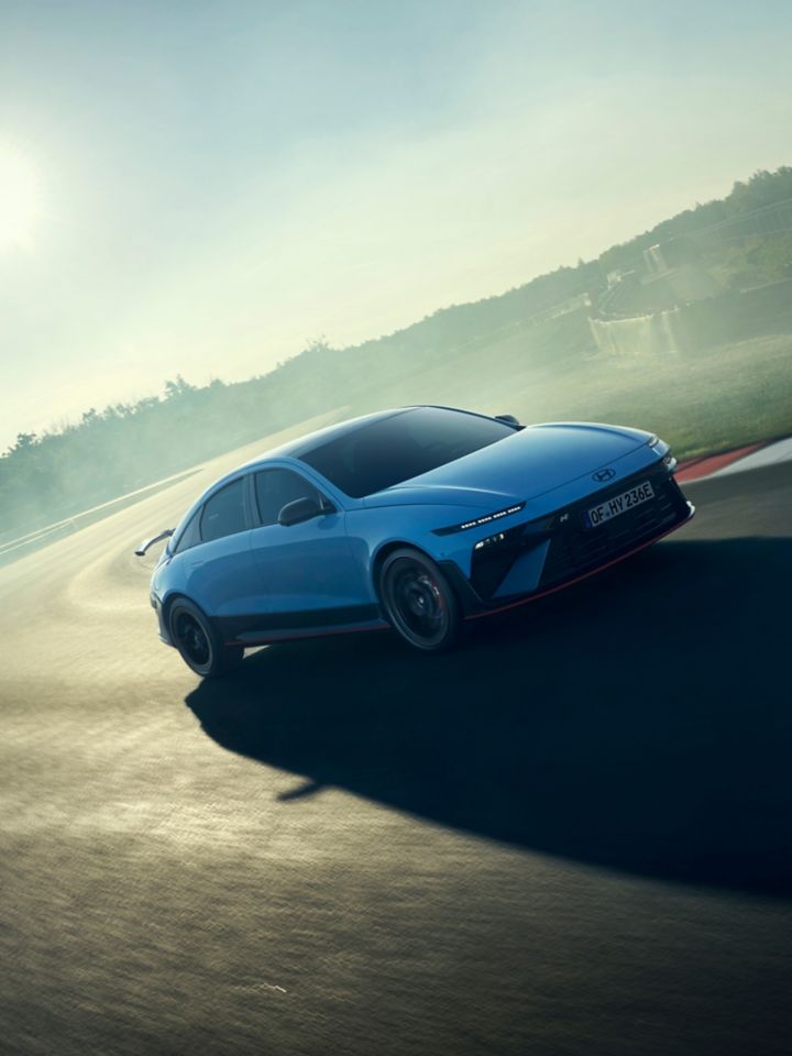 A Hyundai IONIQ 6 N powers through a track corner, showcasing its performance in a misty environment.