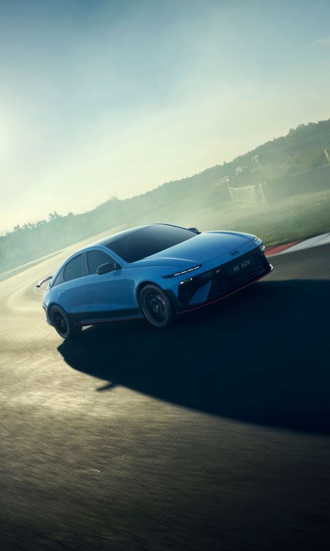 Hyundai i30 seen from rear three-quarter driving on a city street in front of modern buildings.