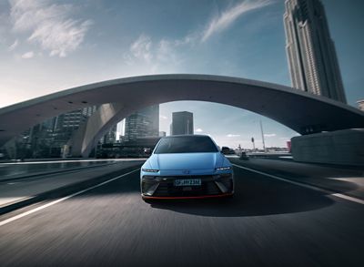 IONIQ 6 N drives under an arching bridge, showcasing its modern design against a cityscape.