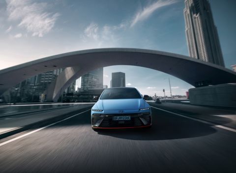 IONIQ 6 N drives under an arching bridge, showcasing its modern design against a cityscape.