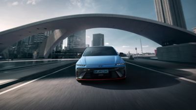 Vooraanzicht van Hyundai IONIQ 6 N rijdend onder een boogbrug, waarbij zijn moderne design afsteekt tegen de stadse omgeving.