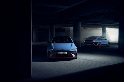 Two Hyundai IONIQ 6 N electric performance sedans in a dimly lit parking garage, front and rear view.