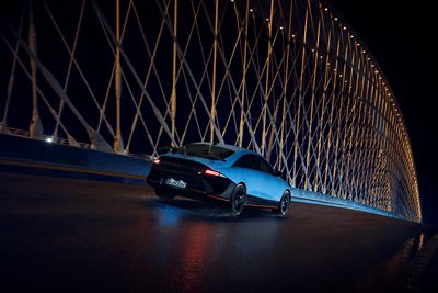 A Hyundai IONIQ 6 N drives across a bridge at night, surrounded by illuminated architectural elements.